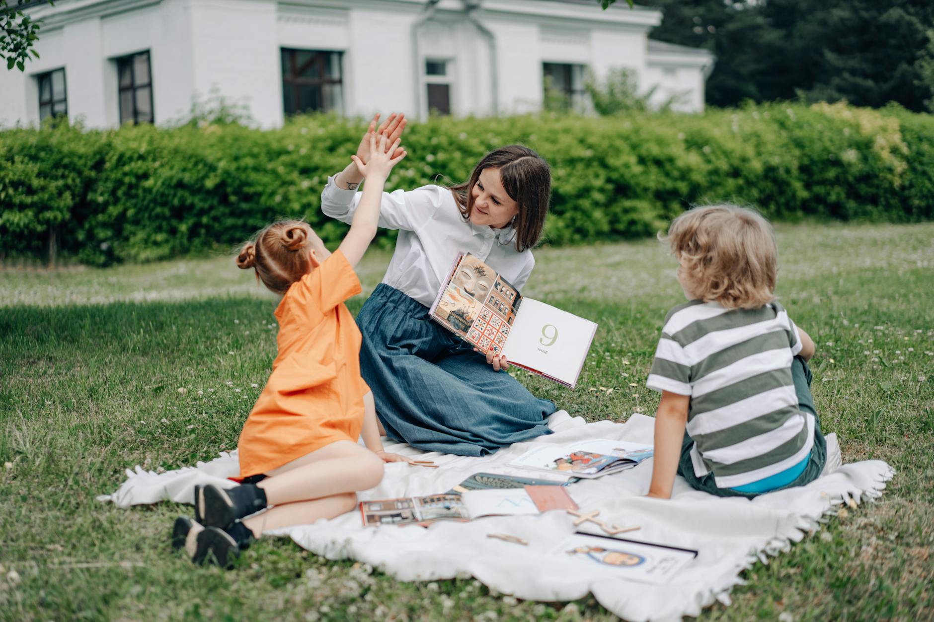Nauczycielka czyta dzieciom książkę na trawie podczas zajęć na dworze