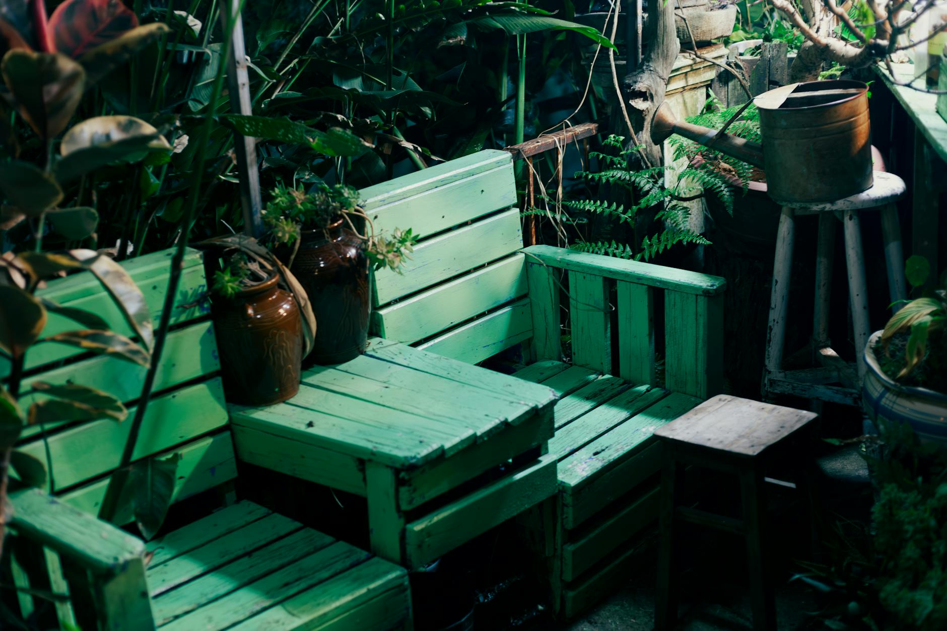 Zielona paletowa ławka w ogrodzie z metalową konewką